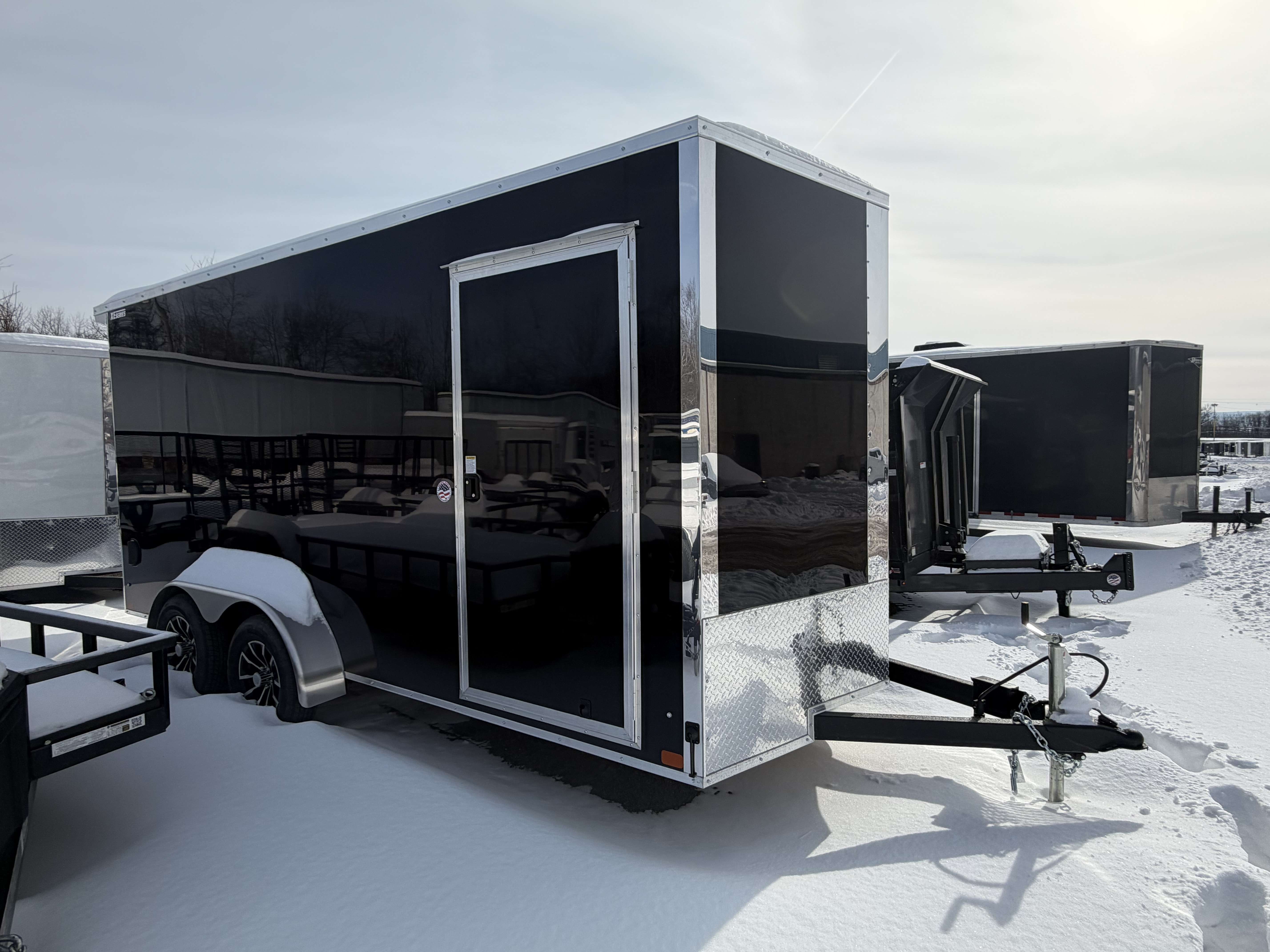 7x16 black enclosed cargo trailer exterior side view in snow with silver trim and aluminum wheels